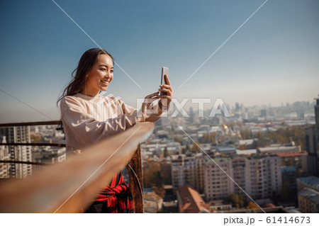 Smiling pretty girl is looking on smartphone screen on roof Smiling pretty girl is looking on smartphone screen on roof 61414673
