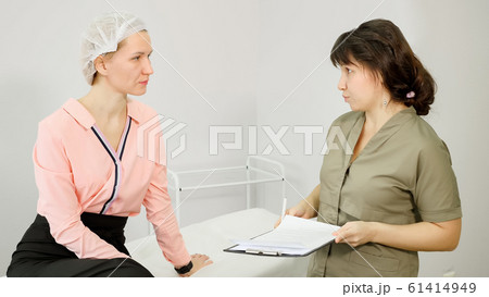 beauty clinic employee in green coat consults young woman 61414949