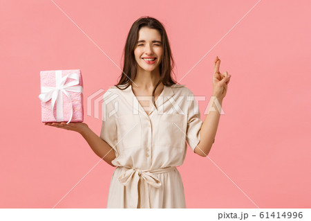Anticipation, celebrating and presents concept. Cute b-day girl in lovely dress making wish, hope find exactly what she wished for inside gift box, cross fingers and close eyes, biting lip tempting 61414996