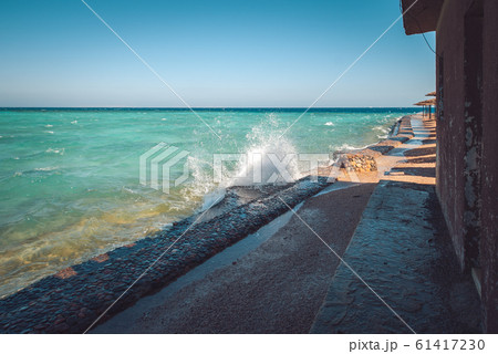 Photo of beautiful clear turquoise sea ocean water surface with ripples and bright splash on stone seascape background, horizontal picture. waves rush to the beach with beach chairs and parasols 61417230