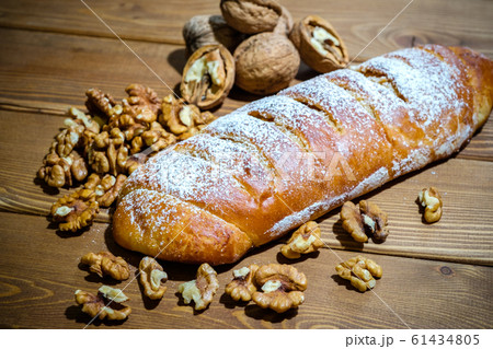 Fresh roll with walnuts and icing sugar on a wooden background. Sweet dessert with nuts on an old table. Fresh roll with walnuts and icing sugar on a wooden background. Sweet dessert with nuts on an old table. 61434805