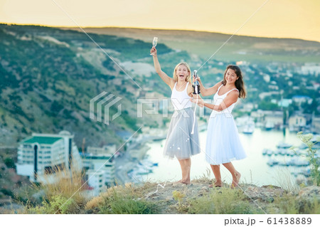 Two happy young women drinking together and having fun on top of a mountain Two happy young women drinking together and having fun on top of a mountain 61438889