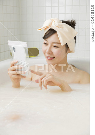 バスルームで防水ケースにスマホを入れて観覧する若い女性 61458119