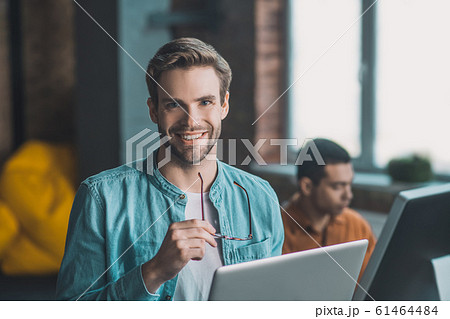 Delighted good looking man standing with his glasses Delighted good looking man standing with his glasses 61464484