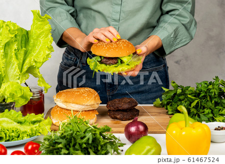 Woman is cooking tasty burger with cutlet, chesse and vegetables in the kitchen. 61467524