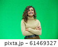 Beautiful woman with kinky hair in beige clothes, isolated on green, looking pleased. 61469327