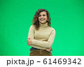 Portrait of a beautiful friendly african american woman with curly hairstyle and lovely smile isolated on a green background, her hands folded. 61469342