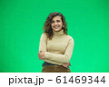 Portrait of a beautiful friendly african american woman with curly hairstyle and lovely smile isolated on a green background, her hands folded. 61469344