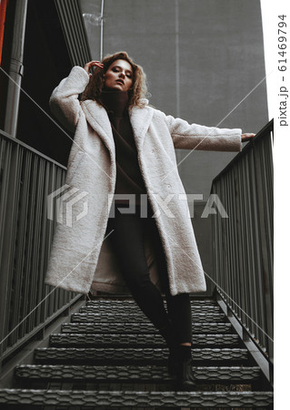 A girl with red curly hair in a white coat poses on the parking stairs A girl with red curly hair in a white coat poses on the parking stairs 61469794