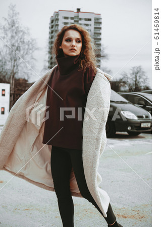 A girl with red curly hair in white coat poses on outdoor parking in cold autumn A girl with red curly hair in white coat poses on outdoor parking in cold autumn 61469814