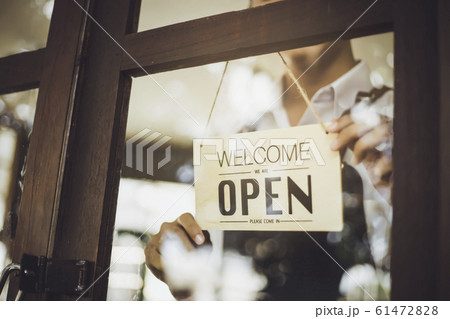 Store owner turning open sign broad through the door glass and ready to service. 61472828