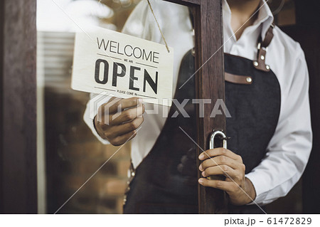 Store owner turning open sign broad through the door glass and ready to service. 61472829