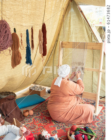Times and Epochs Festival. Female Weaver Weaves a Canvas With a Pattern of Wool Yarn. Woman Weaves Using a Traditional Wooden Loom Times and Epochs Festival. Female Weaver Weaves a Canvas With a Pattern of Wool Yarn. Woman Weaves Using a Traditional Wooden Loom 61473682