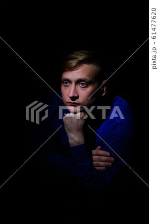 portrait of a handsome young man in a sad shirt sits propping his beard with his hand on a black background portrait of a handsome young man in a sad shirt sits propping his beard with his hand on a black background 61477620