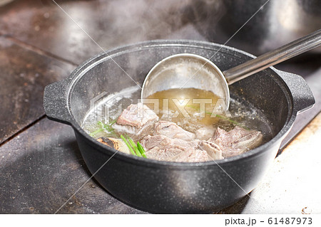 chef cook adds the ingredients. traditional beef broth with vegetable, bones and ingredients in pot, cooking recipe. Soup in a cooking pot with ladle on dark stone background. Top view 61487973