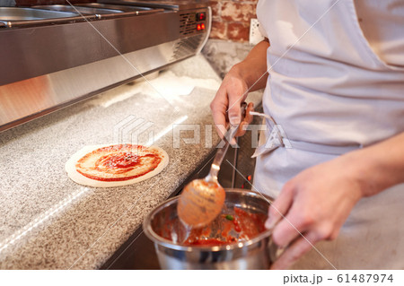 Cooking pizza. the workpiece poured tomato sauce. Closeup hand of chef. Baker in uniform and white apron cooking at kitchen 61487974
