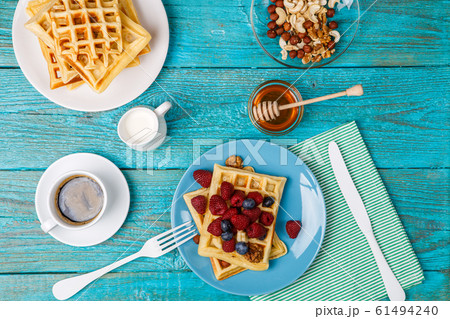 Homemade waffles with raspberries and blueberry, cup of coffee, milk and cutlery Homemade waffles with raspberries and blueberry, cup of coffee, milk and cutlery 61494240