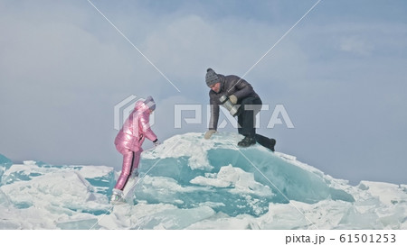 Couple has fun during winter walk against background of ice of frozen lake. Lovers lie on clear ice, have fun, kiss and hug. View from above. 61501253