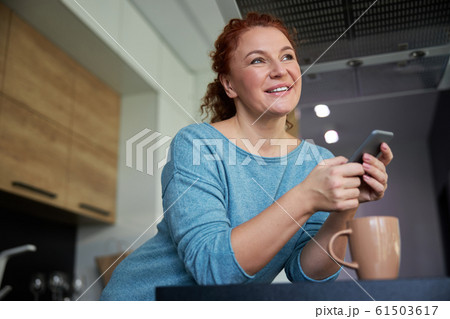 Woman relaxing with smartphone and tea in kitchen stock photo Woman relaxing with smartphone and tea in kitchen stock photo 61503617