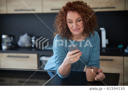 Jolly female with phone and coffee at home stock photo Jolly female with phone and coffee at home stock photo 61504130