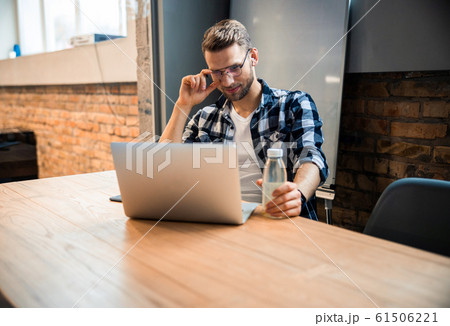 Smiling young guy touching glasses while working in co-working space Smiling young guy touching glasses while working in co-working space 61506221