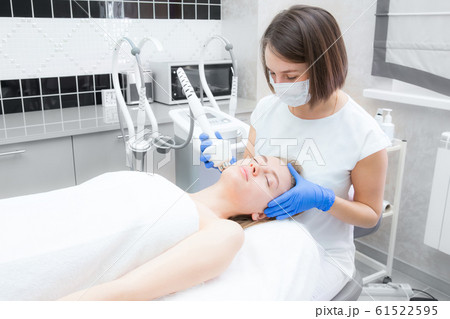 Beautician doctor doing rf-lifting procedure for flawless woman face laying in a beauty salon. Patient receiving electric facial massage. Skin rejuvenation and wrinkle smoothing. Beautician doctor doing rf-lifting procedure for flawless woman face laying in a beauty salon. Patient receiving electric facial massage. Skin rejuvenation and wrinkle smoothing. 61522595
