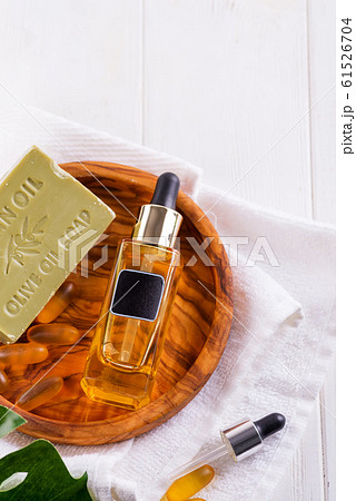Cosmetic bottle with serum or hyaluronic acid and olive soap, Omega-3 gel capsules on wooden plate , palm leaf, on a white towel 61526704