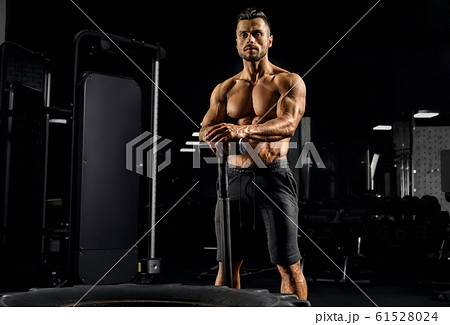 Caucasian shirtless man leaning on sledgehammer. 61528024