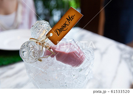 Beautiful crystal glass bottle with lid or stopper on ice crystal bowl with pink love or magical potion or liquor drink inside and vintage tag drink me from Alice in wonderland.  61533520