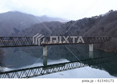 冬のダム湖を渡る電車 61540173