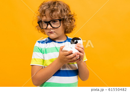 Little boy with curly hair in colourful t-shirt and shorts holds a toy isolated on yellow background 61550482