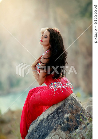 A woman in a red Oriental dress sits on a rock from a cliff A woman in a red Oriental dress sits on a rock from a cliff 61556503