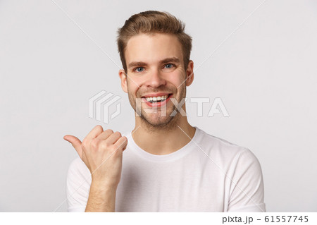 Close-up studio portrait blond handsome and joyful, smiling man asking friend opinion as pointing thumb left, discuss company product, grinning cheerful, standing white background 61557745