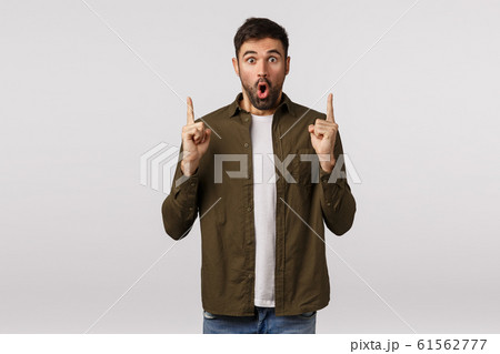 You must see this, wow. Amazed impressed and excited modern bearded male in coat, pointing up, folding lips thrilled, telling interesting news, showing friends great promo offer, discounts 61562777