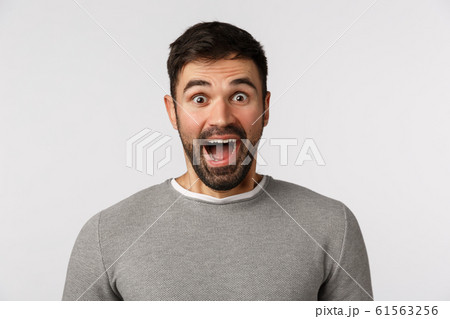 Extremely happy and cheerful good-looking bearded caucasian male in grey sweater, open mouth fascinated, say wow astonished and amused, visit amusement park, express awe and happiness 61563256