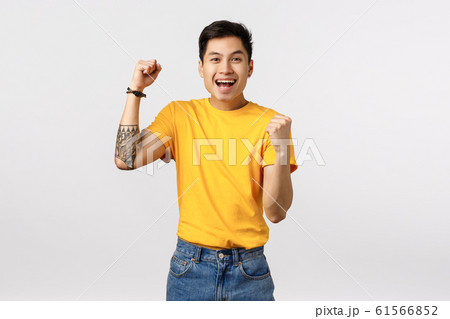 Hooray, well done good for you. Cheerful asian young tattooed man in yellow t-shirt, fist pump encouraging, rooting for player, placed bid, smiling rejoice, become champion, celebrating victory 61566852