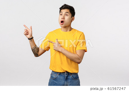 Shocked and alarmed asian guy see someone made incredible stunt, drop jaw, open mouth and stare, pointing upper left corner, standing stupor from shook and amazement, watching interesting performance 61567247