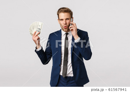Guy telling about greatest achievement over phone, holding big cash, lots dollars money and talking using smartphone, discuss great prize, winning bid at fundraiser, standing white background 61567941