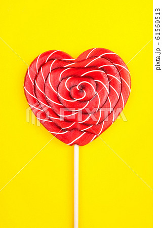 A heart-shaped lollipop on a yellow background. 61569513