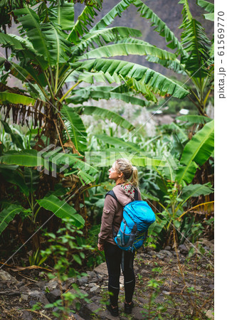 Blond young women with blue backpack admire banana plantation on the trekking route to paul valley on santo antao island, cape verde 61569770