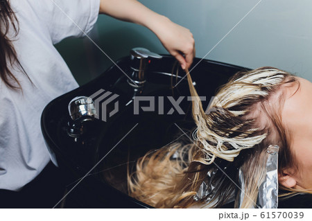Closeup of hairdresser hands separating strands of hair of beautiful young woman with aluminium foil before change the hair color. Closeup of hairdresser hands separating strands of hair of beautiful young woman with aluminium foil before change the hair color. 61570039