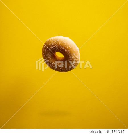Sugar doughnut in motion falling on yelloy background Sugar doughnut in motion falling on yelloy background 61581315