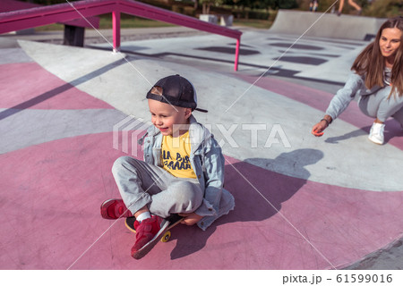 Little boy 3-5 years old, riding skateboard, rest on weekend, education and training, first steps on board. In summer in city. Casual clothes, jeans with a hood. Happy smiling rejoices and has fun. 61599016