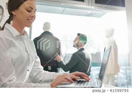 Young smiling shop assistant looking through online assortment on laptop screen 61599793
