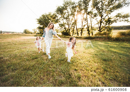 Blonde mother with two cute daughters are walking and having fun outdoors. Stylish, casual clothes. Blonde mother with two cute daughters are walking and having fun outdoors. Stylish, casual clothes. 61600908