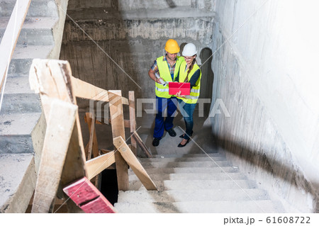 Construction worker and builder inspecting stairs in building shell Construction worker and builder inspecting stairs in building shell 61608722