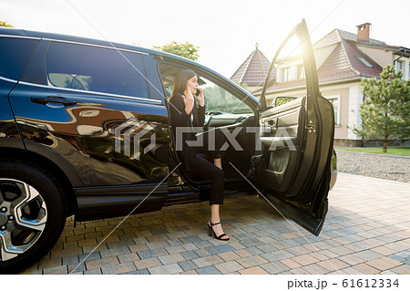 Beautiful emotional business woman is talking on the mobile phone, while sitting on the passenger seat in the car with open door 61612334