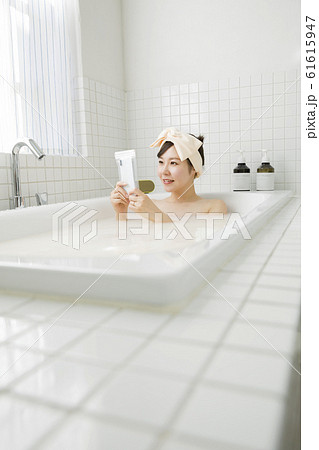 バスルームで防水ケースにスマホを入れて観覧する若い女性 61615947