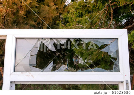 Window frame with broken glass on the background of trees in the city Park. 61628686
