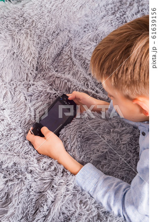 Young boy playing handheld game console against grey sheepskin rug background 61639156